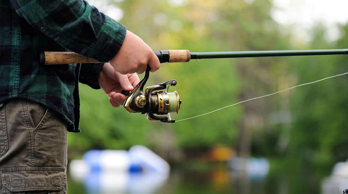 Angler in a green plaid shirt holding a spinning rod and reel by a lake